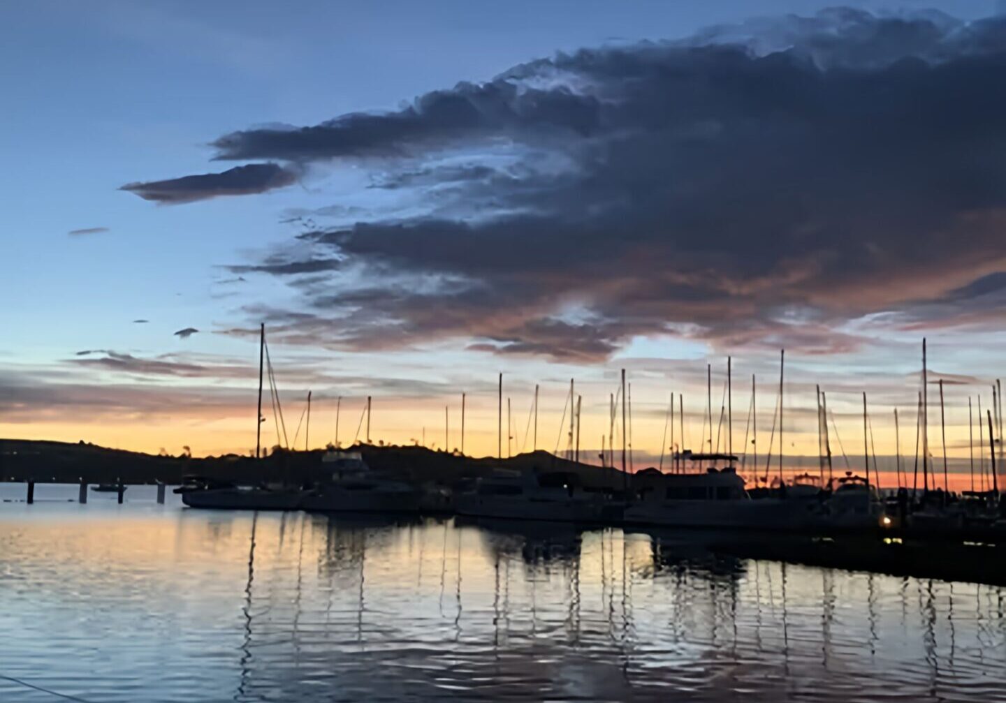 Sunset over a calm marina with silhouetted sailboats.